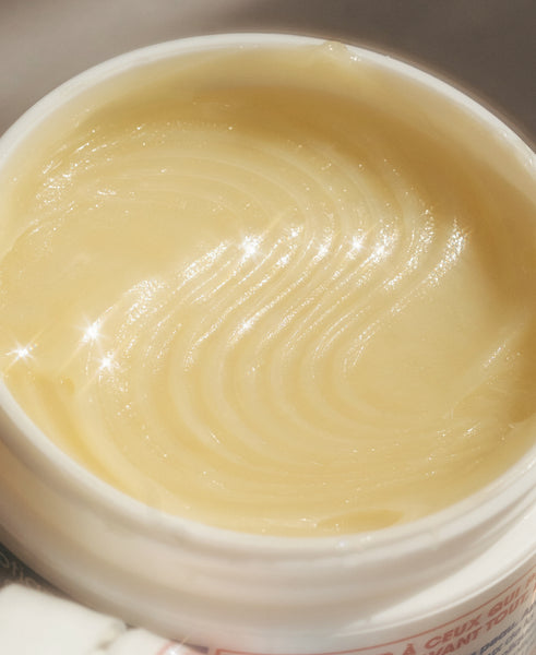 Close-up of a white cosmetic jar filled with a pale creamy yellow balm or cream, showing a swirled texture on the surface.