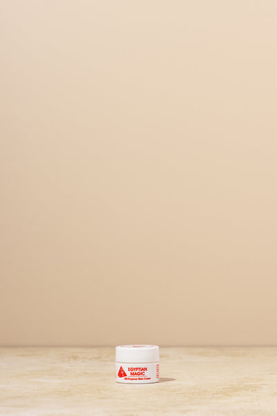 A small white cosmetic jar labeled 'Egyptian Magic' sits on a light beige surface against a matching beige background.